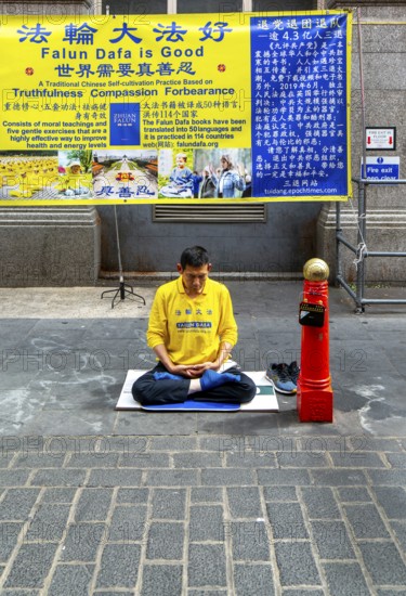 Falun Dafa or Falun Gong man meditating sitting cross legged, Gerrard Street, Chinatown, West End, London, England, UK