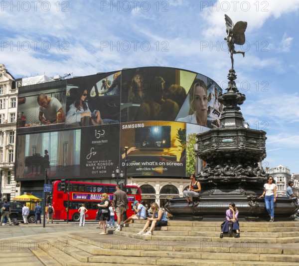 People sitting around Eros statue, Piccadilly Circus, central London, England, UK - Shaftesbury Memorial Fountain