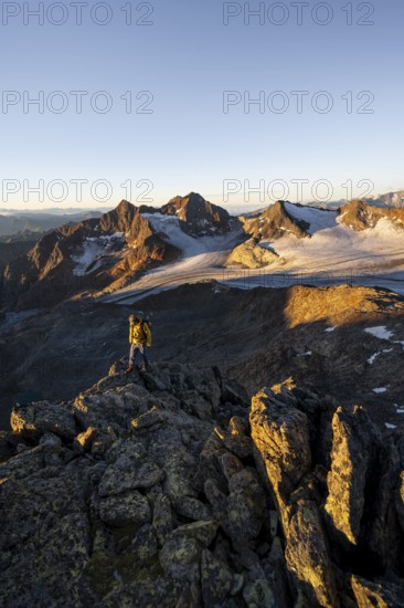 Mountaineers in front of a picturesque high mountain landscape at sunrise with alpenglow, glacier and rocky mountain peaks in the morning light, view at the Becher on mountain peak Königshofspitz and glacier Übeltalferner, Stubai Alps, South Tyrol, Italy