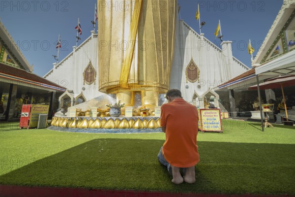 Man praying in front of a 32 metre high standing Buddha decorated with glass mosaics and 24 carat gold, Luang Pho To or Phrasiariyametri, Wat Intharawihan, Bangkok, Thailand
