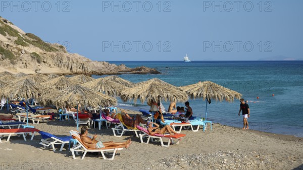 Beach scene with deckchairs and beach mats under umbrellas near the sea, Agios Stefanos Beach, Agios Stefanos Basilica, Chapel of Agios Nikolaos, Kastri Island, Kos, Dodecanese, Greek Islands, Greece
