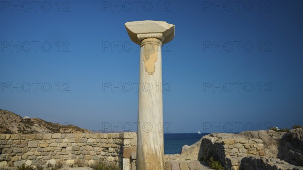 Freestanding stone column in front of a historical site with blue sky in the background, Agios Stefanos Beach, Agios Stefanos Basilica, Chapel of Agios Nikolaos, Kastri Island, Kos, Dodecanese, Greek Islands, Greece