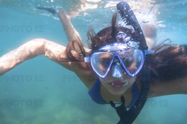 Tourist enjoys snorkeling in crystal clear ocean water, creating a stream of bubbles as she breathes through her snorkel
