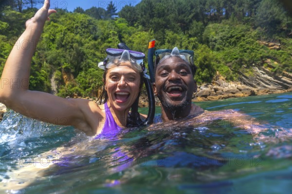 Interracial couple wearing snorkeling masks enjoys swimming in the ocean during summer vacation, having fun together