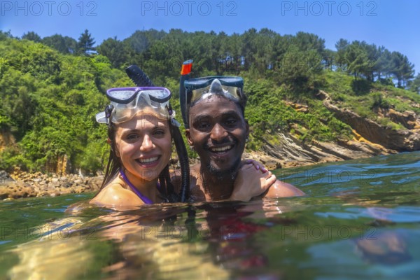 Interracial couple snorkeling in the clear blue sea, surrounded by a stunning green cliff, enjoying a joyful summer adventure together