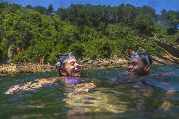 Tourists wearing snorkeling masks, laughing joyfully while enjoying a sunny summer vacation in the crystal clear ocean waters
