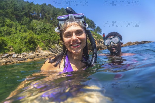 Happy couple snorkeling together in the ocean near the rocky coastline, enjoying their summer vacation
