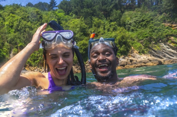Interracial couple enjoying a fun snorkeling adventure in the vibrant ocean, laughing and sharing joyful moments during a summer vacation