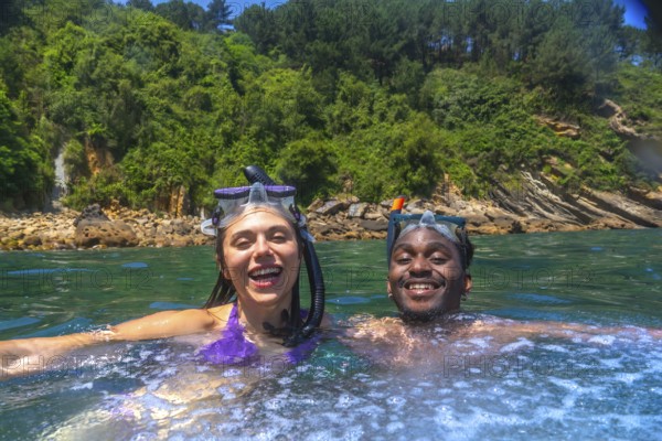 Interracial couple enjoying snorkeling in beautiful turquoise water with lush vegetation on the background