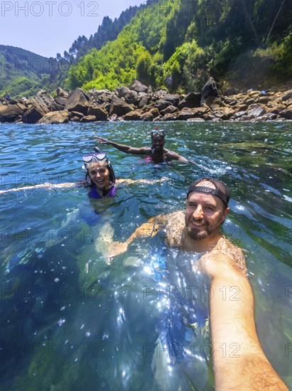 Three friends wearing snorkeling gear and enjoying the refreshing ocean water near a rocky coast