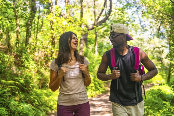 Young multi ethnic couple enjoying a hike together, walking and talking on a sunny trail in a lush green forest