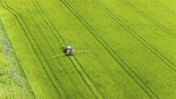 Farmer with tractor working in the field. In early summer, he fertilises the grain for an optimum yield. Drone photo. Merklingen, Baden-Württemberg, Germany