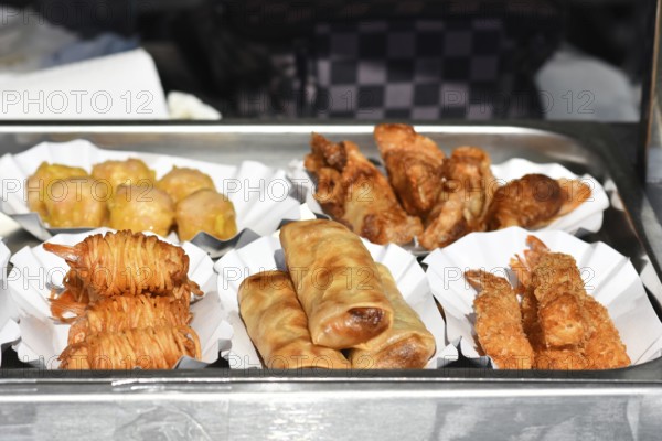 Different small fried Thai street food snacks like fried shrimp, springrolls or potato noodle prawns on small trays