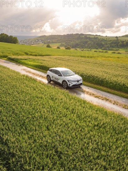 A car drives on a dirt track through a rape field under a cloudy sky, Deer E- CarSharing, Renault Megane electric car, Calw, Black Forest, Germany
