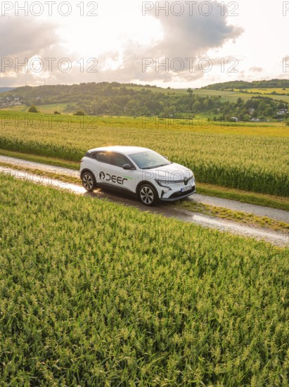A car drives on a country lane through wide green meadows under a cloudy sky, Deer E- CarSharing, Renault Megane electric car, Calw, Black Forest, Germany