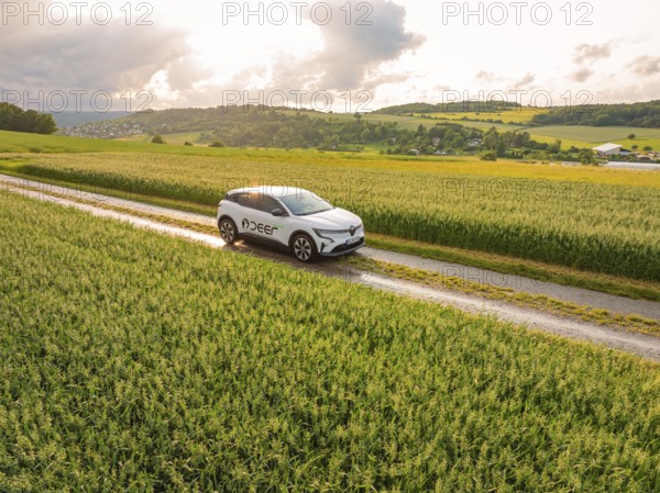 A car moves along a path through green fields with a wide view of the landscape, Deer E- CarSharing, Renault Megane electric car, Calw, Black Forest, Germany