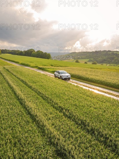 A car drives on a narrow road along green fields under a cloudy sky, Deer E- CarSharing, Renault Megane electric car, Calw, Black Forest, Germany