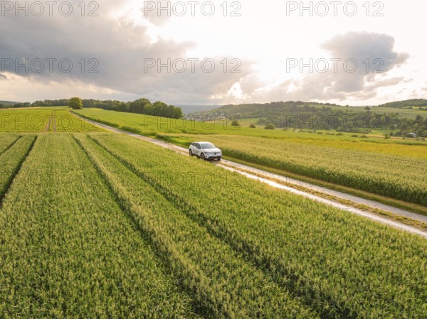Country lane with a car, surrounded by cornfields and a dramatic sky, Deer E- CarSharing, Renault Megane electric car, Calw, Black Forest, Germany