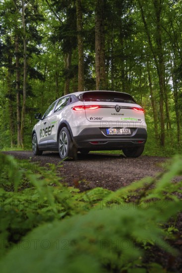 Car on forest road with shining rear lights surrounded by dense green forest, Deer E- CarSharing, Renault Megane electric car, Calw, Black Forest, Germany