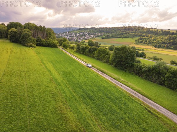 Car drives a straight road through wide green landscape with cloudy sky, Deer E- CarSharing, Renault Megane electric car, Calw, Black Forest, Germany