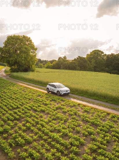 A car drives on a dirt track between green fields under a cloudy sky, Deer E- CarSharing, Renault Megane electric car, Calw, Black Forest, Germany