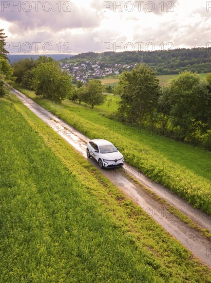 Car drives on narrow road through green landscape with village on the horizon, Deer E- CarSharing, Renault Megane electric car, Calw, Black Forest, Germany