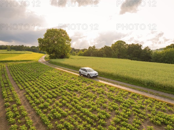 A car drives on a dirt road through an agricultural area with a cloudy sky, Deer E- CarSharing, Renault Megane electric car, Calw, Black Forest, Germany