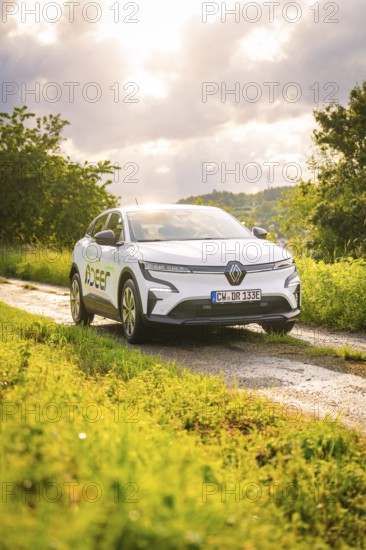White car on a rural road with green meadows and cloudy sky in the background, Deer E- CarSharing, Renault Megane electric car, Calw, Black Forest, Germany