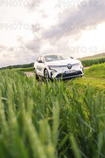 White car surrounded by vegetation and fields under a partly cloudy sky, Deer E- CarSharing, Renault Megane electric car, Calw, Black Forest, Germany