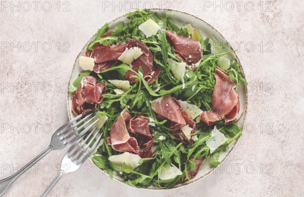 Fresh arugula salad with prosciutto and grated parmesan cheese, on a plate, homemade, no people