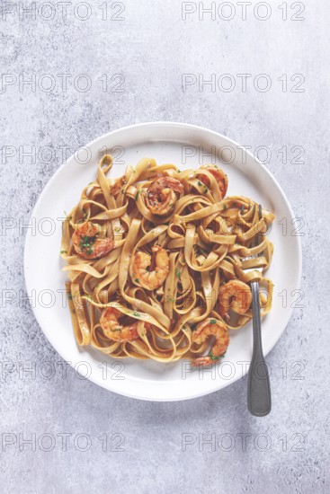 Fettuccine pasta with shrimp, spicy in soy sauce, on a grey plate with a fork, close-up