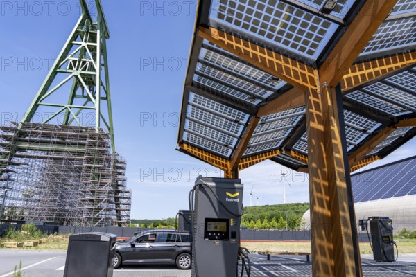 Electric filling station on the site of the former Lohberg colliery in Dinslaken, operated by Fastned, uses electricity from wind power and solar energy, fast-charging columns, with its own solar roof, in the background the 11, 500 square metre solar roof on the colliery's former coal mixing hall, wind farm on the Lohberg slagheap, Lohberg colliery headframe, North Rhine-Westphalia, Germany