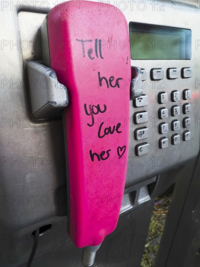 Telephone receiver of a Telekom payphone with the inscription Tell her you love her in Wuppertal, Germany