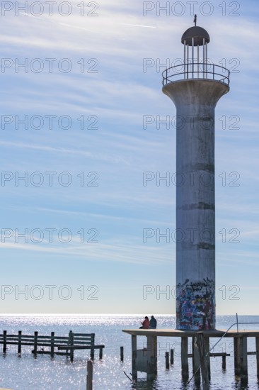 Man and woman sitting on a concrete platform at the base of the graffiti, covered Broadwater Beach Marina Light in Biloxi, MS