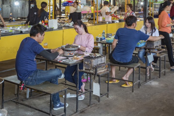 Thai couple cooking on a hot pot and eating at a buffet style outdoor restaurant in Chiang Rai province of Northern Thailand