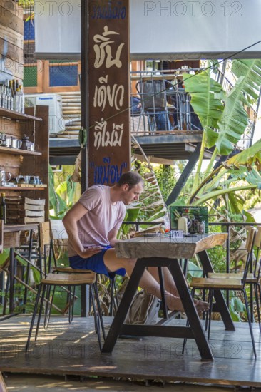 Restaurant customer reading a book while waiting for his order at the Akha Cottage restaurant and coffee shop in Chiang Rai, Thailand