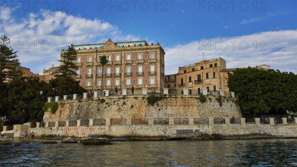 Elevated wall with historic buildings and lush vegetation in the coastal area, boat trip around the island of Ortigia, Isola di Ortigia, Syracuse, Sicily, Italy