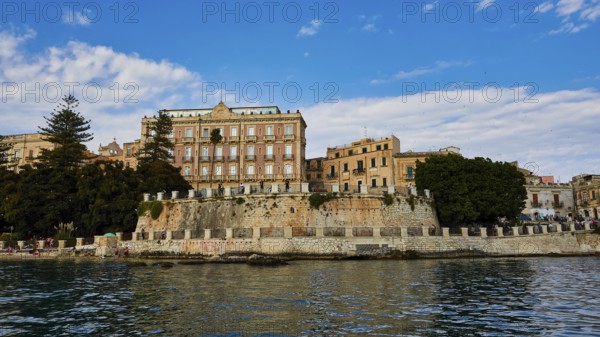 Magnificent old buildings with trees rising above the calm water, boat trip around the island of Ortigia, Isola di Ortigia, Syracuse, Sicily, Italy