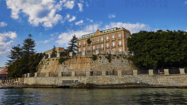 Magnificent building on a cliff, surrounded by lush vegetation and clear skies, boat trip around the island of Ortigia, Isola di Ortigia, Syracuse, Sicily, Italy