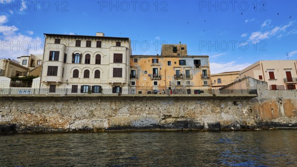 Historic buildings along a stone seawall under an expansive blue sky, boat trip around the island of Ortigia, Isola di Ortigia, Syracuse, Sicily, Italy