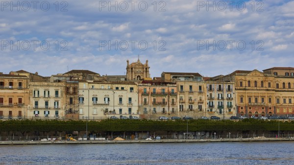Rows of historic buildings along a coastal promenade under a patterned sky, boat trip around the island of Ortigia, Isola di Ortigia, Syracuse, Sicily, Italy