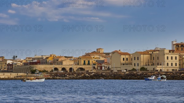 Town by the sea with old buildings and small boats, blue sky above, boat trip around the island of Ortigia, Isola di Ortigia, Syracuse, Sicily, Italy