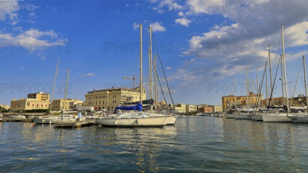 Several sailing boats moored in a marina, surrounded by a sunny city view, boat trip around the island of Ortigia, Isola di Ortigia, Syracuse, Sicily, Italy