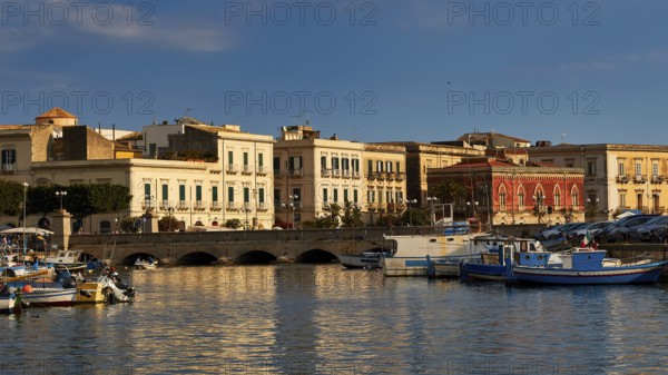 Harbour with fishing boats and colourful historic buildings in the warm evening light, boat trip around the island of Ortigia, Isola di Ortigia, Syracuse, Sicily, Italy
