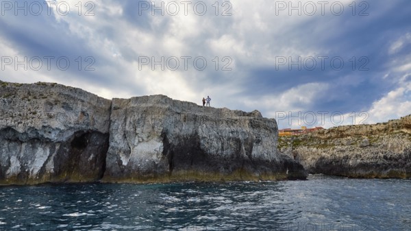 People standing on cliffs under a dramatic sky by the sea, boat trip around the island of Ortigia, Isola di Ortigia, Syracuse, Sicily, Italy