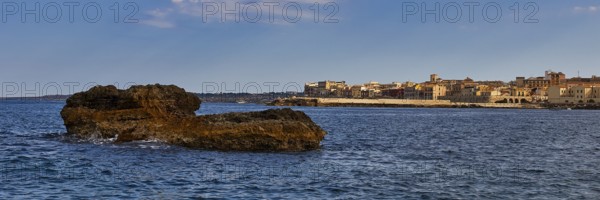 Coastal cliffs in the foreground with a town and blue sky in the background, boat trip around the island of Ortigia, Isola di Ortigia, Syracuse, Sicily, Italy