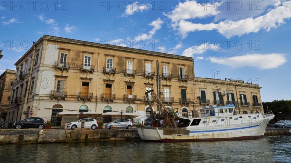 Historic coastal building with parked boat under a blue sky, boat trip around the island of Ortigia, Isola di Ortigia, Syracuse, Sicily, Italy