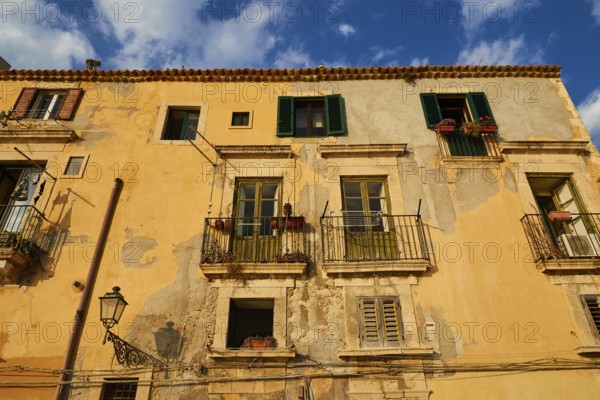 Shows the weather-beaten facade of a building with balconies and windows, blue sky above, Ortigia Island, Isola di Ortigia, Historic Centre, Syracuse, Sicily, Italy