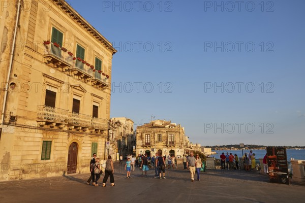 People and historic buildings on a sunny town square in the evening, Ortigia Island, Isola di Ortigia, Historic city centre, Syracuse, Sicily, Italy