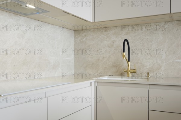 Modern minimalistic kitchen design with light stone surfaces and golden faucet